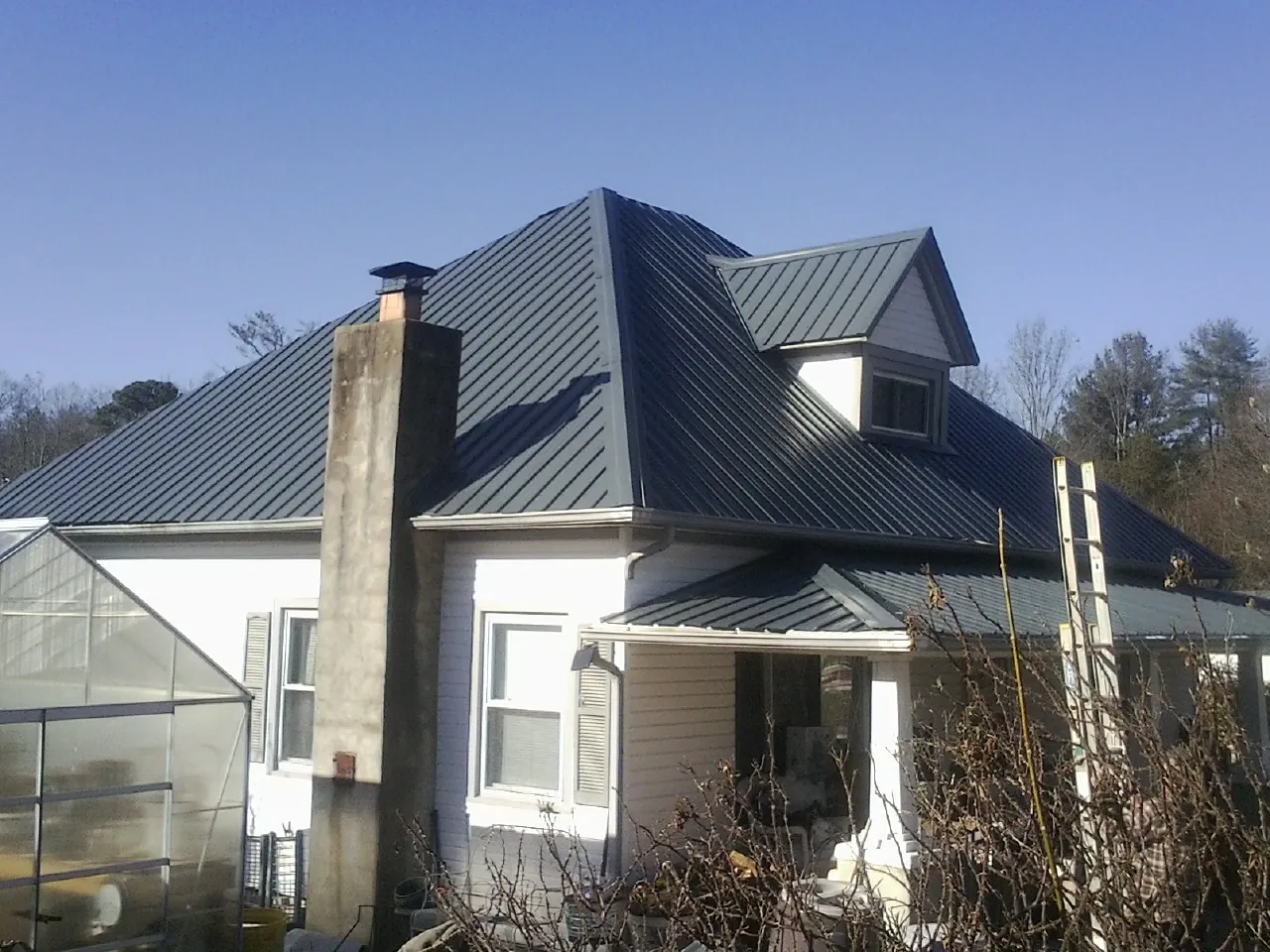 Dark blue standing seam metal roof on a white farmhouse with dormer — Slate & Tile Roof Repair by Roofing Brothers in Fenton
