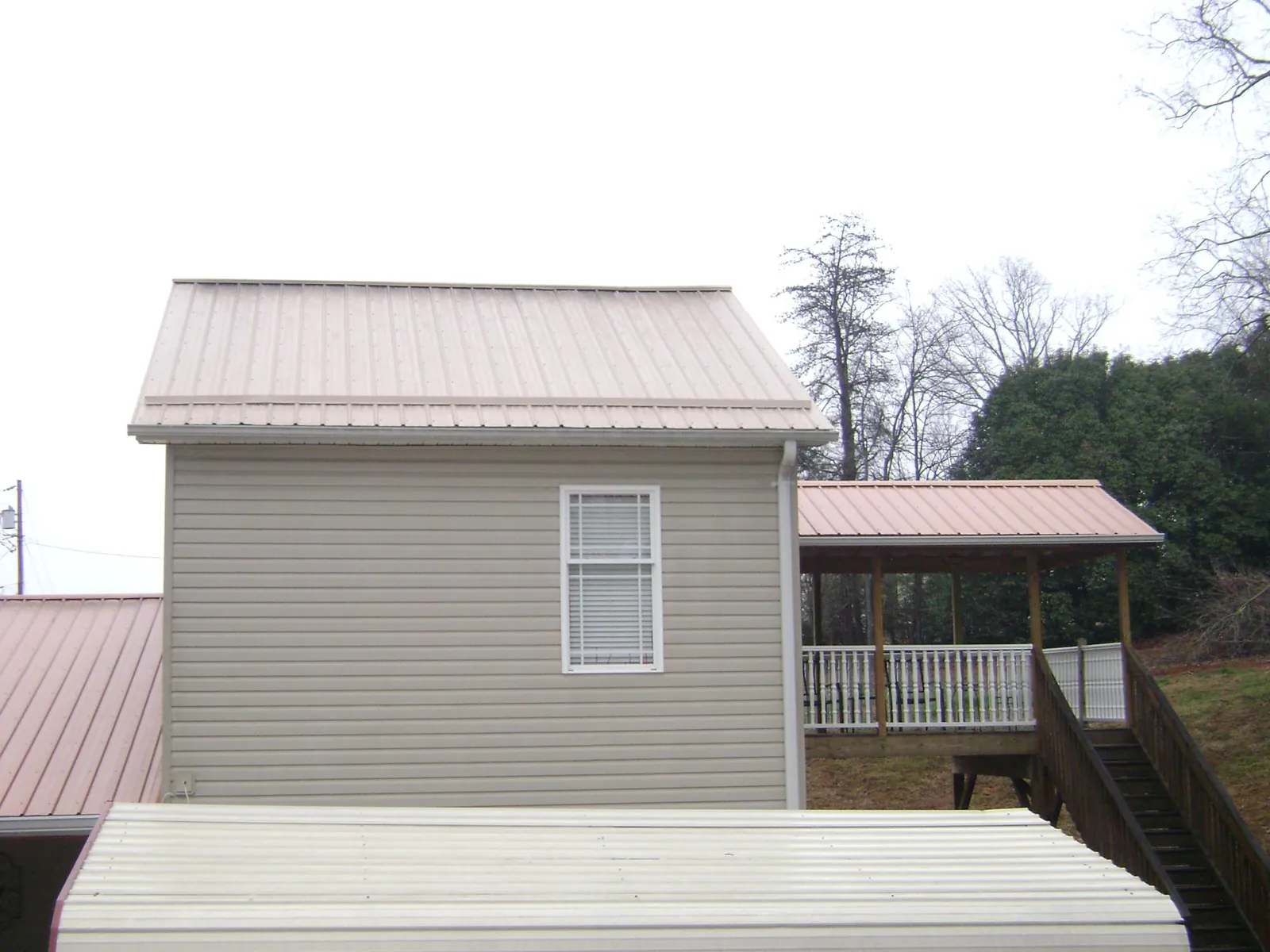 Tan metal roofs on a two story addition and attached porch, from a Roof Replacement job in Fenton